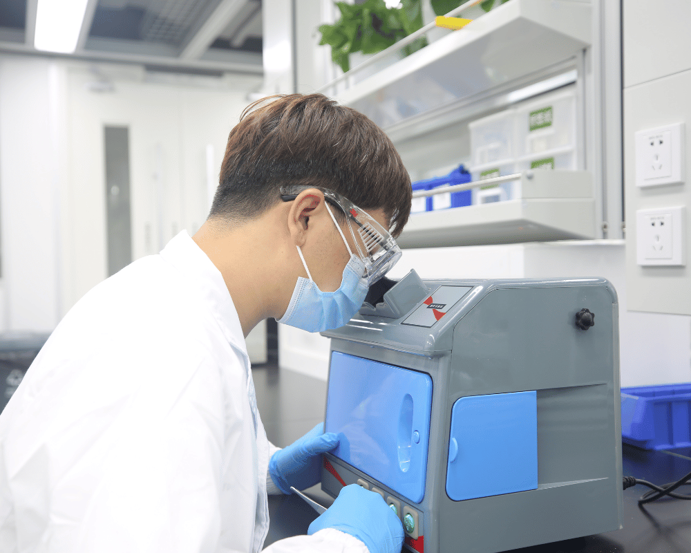 Laboratory scientist in white lab coat viewing crystallization sample inside benchtop UV inspection box.