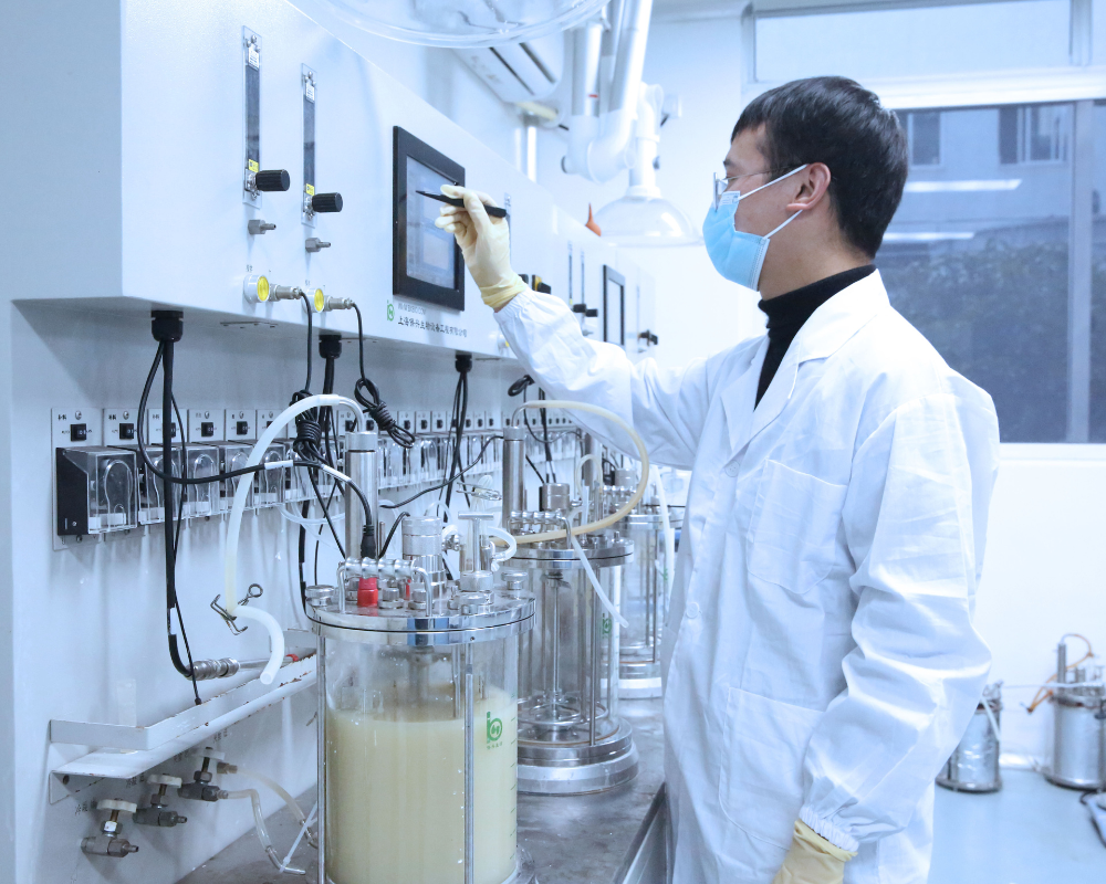 An Apeloa lab scientist in a white lab coat adjusting the control panel on fermentation lab equipment.