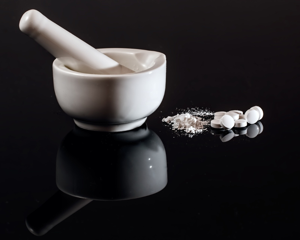 White mortar and pestle with pharmaceutical tablets and powder blend on a black background.