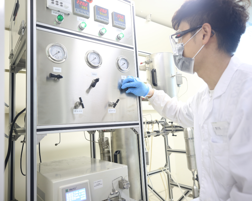 Scientist in white lab coat and blue glove using controls on stainless steel control panel in CRO R&D laboratory.